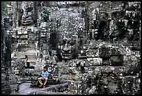 Boy sits next to large stone smiling faces, the Bayon. Angkor, Cambodia ( color)