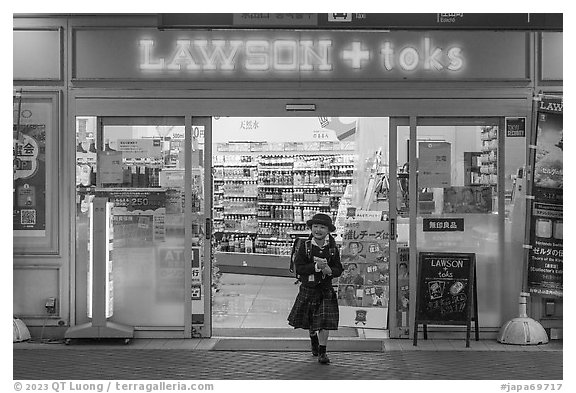 Girl in school uniform walking out of convenience store. Tokyo, Japan (black and white)