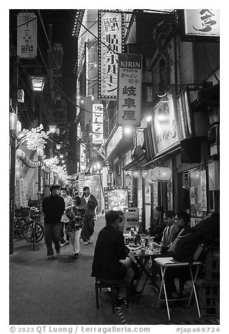 Dinners at outside table in alley at night, Shinjuku. Tokyo, Japan (black and white)