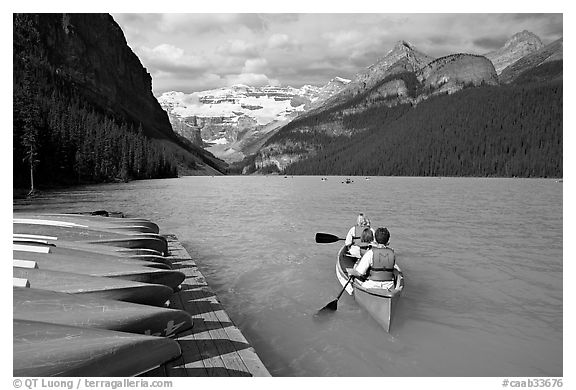 Canoeists paddling out of the boat dock in blue-green waters, Lake Louise, morning. Banff National Park, Canadian Rockies, Alberta, Canada (black and white)