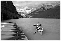 Canoeists paddling out of the boat dock in blue-green waters, Lake Louise, morning. Banff National Park, Canadian Rockies, Alberta, Canada (black and white)