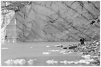 Hikers on the shore of Cavell Pond with high glacier wall behind. Jasper National Park, Canadian Rockies, Alberta, Canada (black and white)