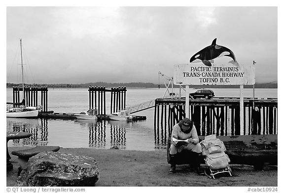 Backpacker sitting under the Transcanadian terminus sign, Tofino. Vancouver Island, British Columbia, Canada (black and white)