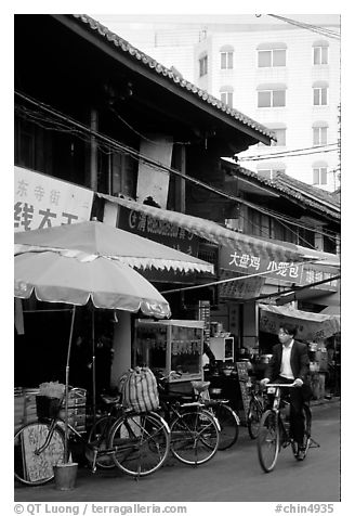 Man on bicycle in front of wooden buildings. Kunming, Yunnan, China (black and white)