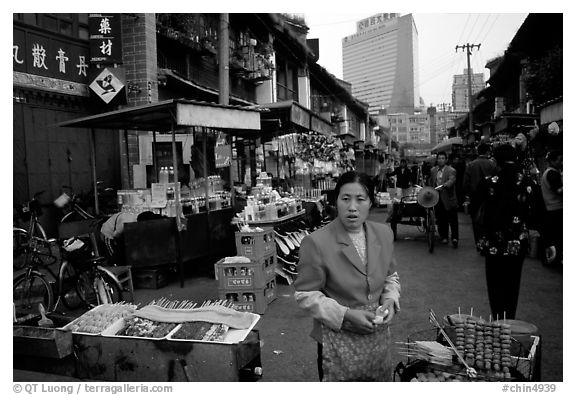Street market in an old alley of wooden buildings, with a high rise in the background. Kunming, Yunnan, China (black and white)