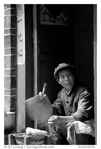 Naxi woman at doorway selling broiled corn. Lijiang, Yunnan, China