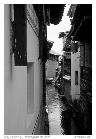 Canal sneaking narrowly between walls. Lijiang, Yunnan, China (black and white)