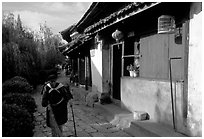 Naxi woman sweeps the floor at the door of her wooden house. Lijiang, Yunnan, China ( black and white)