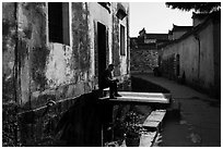 Man sitting in front of house on bridge over stream. Xidi Village, Anhui, China ( black and white)