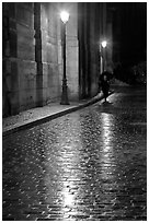 Street lamps reflected in wet pavement, with woman walking. Paris, France (black and white)