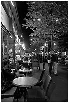 Couple walking by outdoor tables of cafe at night. Paris, France (black and white)