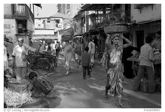 Women carrying  baskets on head in narrow street, Colaba Market. Mumbai, Maharashtra, India (black and white)