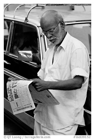 Man reading newspaper next to taxi. Mumbai, Maharashtra, India (black and white)