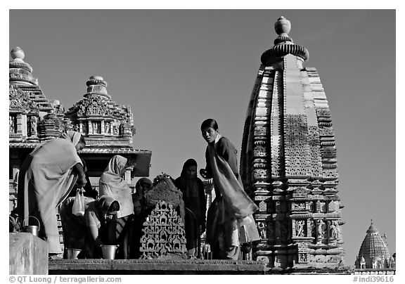 Women worshipping image with of Vahara and Lakshmana temples behind. Khajuraho, Madhya Pradesh, India (black and white)