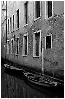 Small boats moored along a wall in a small side canal. Venice, Veneto, Italy (black and white)