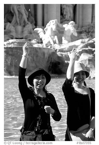 Asian tourists toss a coin over their shoulder into the Trevi Fountain. Rome, Lazio, Italy (black and white)