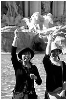 Asian tourists toss a coin over their shoulder into the Trevi Fountain. Rome, Lazio, Italy (black and white)