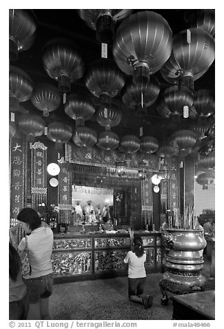 Woman in prayer, altar and lanters, Kuan Yin Teng temple. George Town, Penang, Malaysia (black and white)