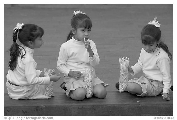 Three little girls in school uniform eating snack. Guadalajara, Jalisco, Mexico (black and white)