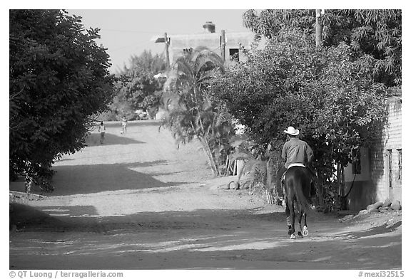 Man on horse going down a village street. Mexico (black and white)