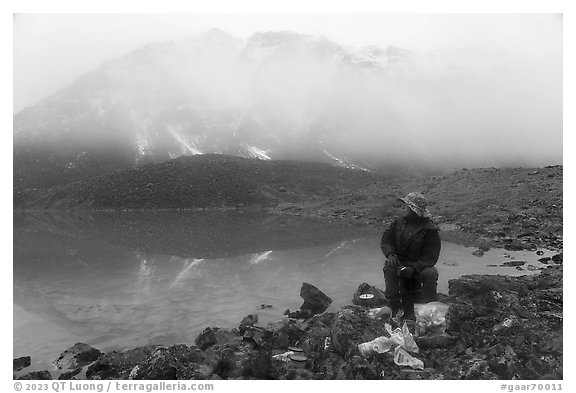 Backpacker eating near lake with foggy mountain. Gates of the Arctic National Park (black and white)
