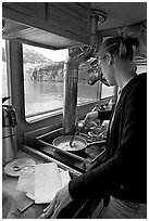 Woman cooking eggs aboard small tour boat, with glacier outside. Glacier Bay National Park, Alaska, USA. (black and white)