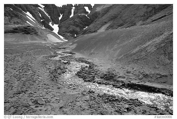 Stream flows from verdant hills into  barren valley floor. Katmai National Park, Alaska, USA.