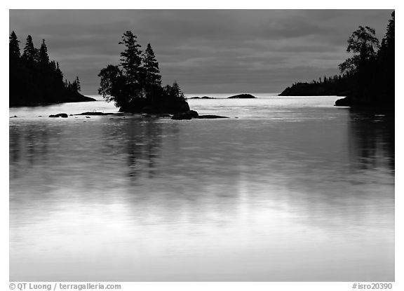 Islet and bright sky reflected in water below dark clouds. Isle Royale National Park (black and white)
