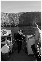Woman diver stepping onto boat and Annacapa Island. Channel Islands National Park, California, USA. (black and white)