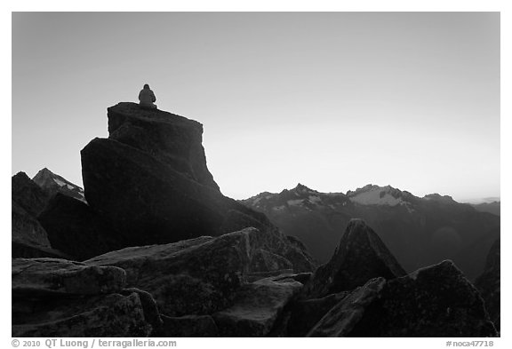 Man sitting on rock contemplates mountains at sunrise, North Cascades National Park.  (black and white)