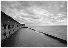 Fort Jefferson brick rampart and moat with wave over seawall, cloudy weather. Dry Tortugas National Park, Florida, USA. (black and white)