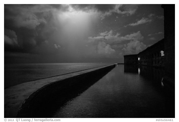 Fort Jefferson seawall at night with sky lit by thunderstorm. Dry Tortugas National Park (black and white)