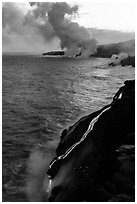 Bright molten lava flows into the Pacific Ocean, plume in background. Hawaii Volcanoes National Park, Hawaii, USA. (black and white)