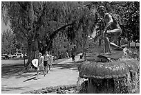 Young men carring surfboards next to statue of surfer, Kapiolani Park. Waikiki, Honolulu, Oahu island, Hawaii, USA ( black and white)