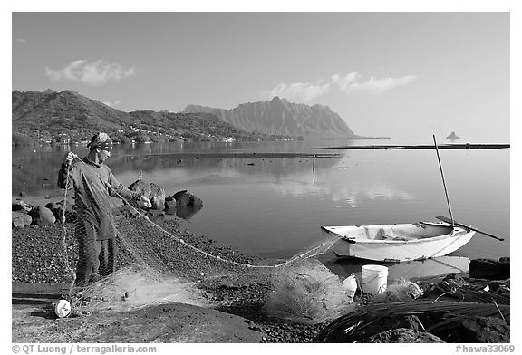 Fisherman pulling out net out of small baot, Kaneohe Bay, morning. Oahu island, Hawaii, USA (black and white)