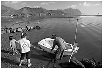 Fisherman and family pulling out net out of small baot, Kaneohe Bay, morning. Oahu island, Hawaii, USA (black and white)