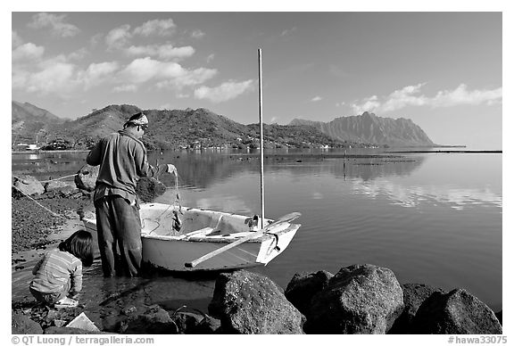 Fisherman pulling out fish out a net as girllooks, Kaneohe Bay, morning. Oahu island, Hawaii, USA (black and white)
