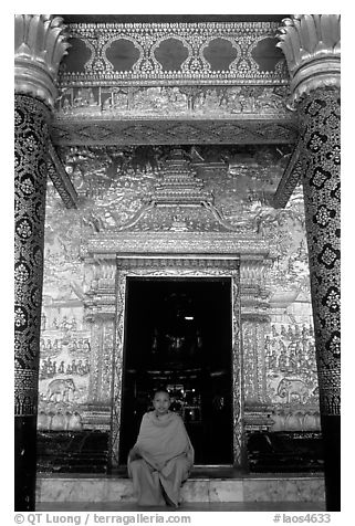 Buddhist novice monk sits at door of Wat Mai Suwannaphumaham. Luang Prabang, Laos (black and white)