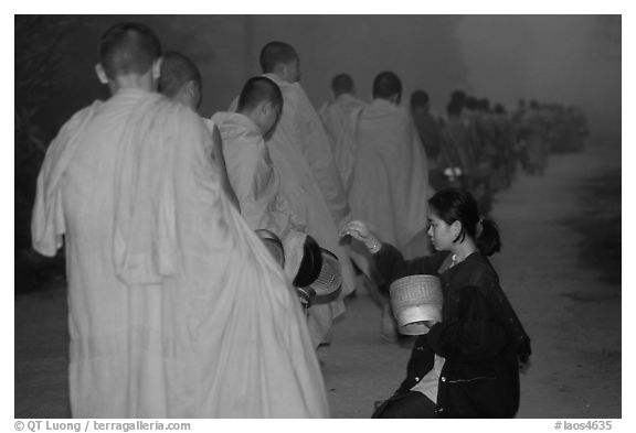 Woman gives alm during morning procession of buddhist monks. Luang Prabang, Laos (black and white)