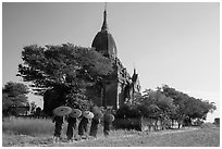 Five novices with red umbrellas walking below temple. Bagan, Myanmar ( black and white)