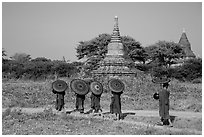 Buddhist Novices with red sun umbrellas on path near old stupas. Bagan, Myanmar ( black and white)
