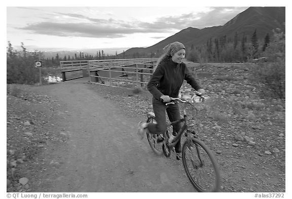 Woman on mountain bike with bridge behind. McCarthy, Alaska, USA