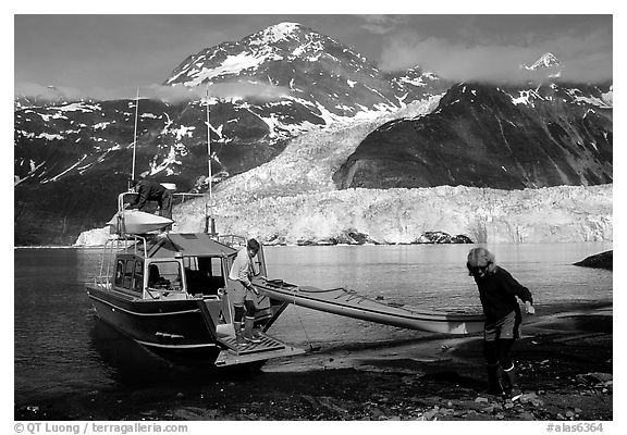 Man and woman  unload  kayak from the water taxi boat at Black Sand Beach. Prince William Sound, Alaska, USA (black and white)