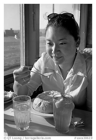 Woman eating a bown of clam chowder on the pier. Santa Cruz, California, USA (black and white)