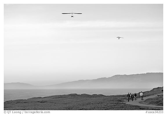Hang gliders soaring above hikers, Fort Funston, late afternoon. San Francisco, California, USA (black and white)