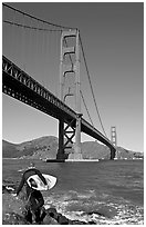Surfer stepping on rocks and Golden Gate Bridge. San Francisco, California, USA (black and white)