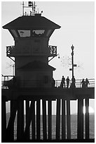 People and pier silhouetted by the setting sun. Huntington Beach, Orange County, California, USA (black and white)
