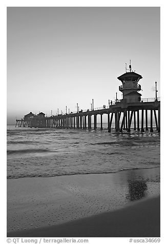 Huntington Pier and reflections in wet sand at sunset. Huntington Beach, Orange County, California, USA (black and white)