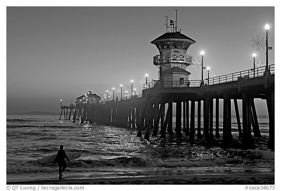 Surfer and Huntington Pier lights at twilight. Huntington Beach, Orange County, California, USA (black and white)