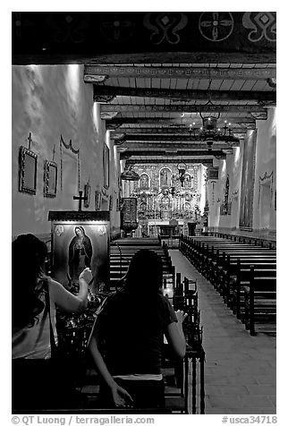 Two women light up candles in the Serra Chapel. San Juan Capistrano, Orange County, California, USA